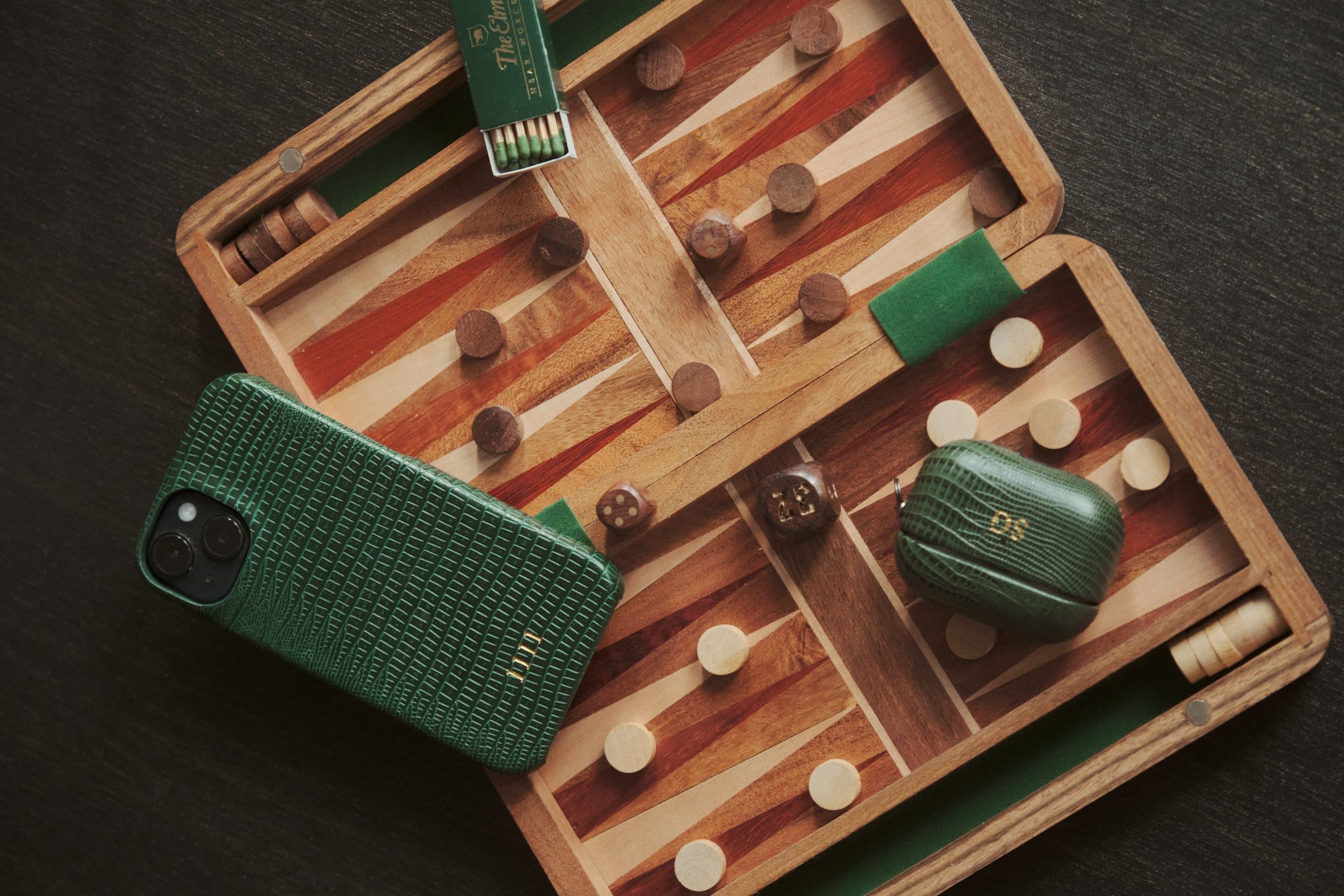 A green lizard-grain phone case and matching accessories by INSÉRIF, laid out on a backgammon board